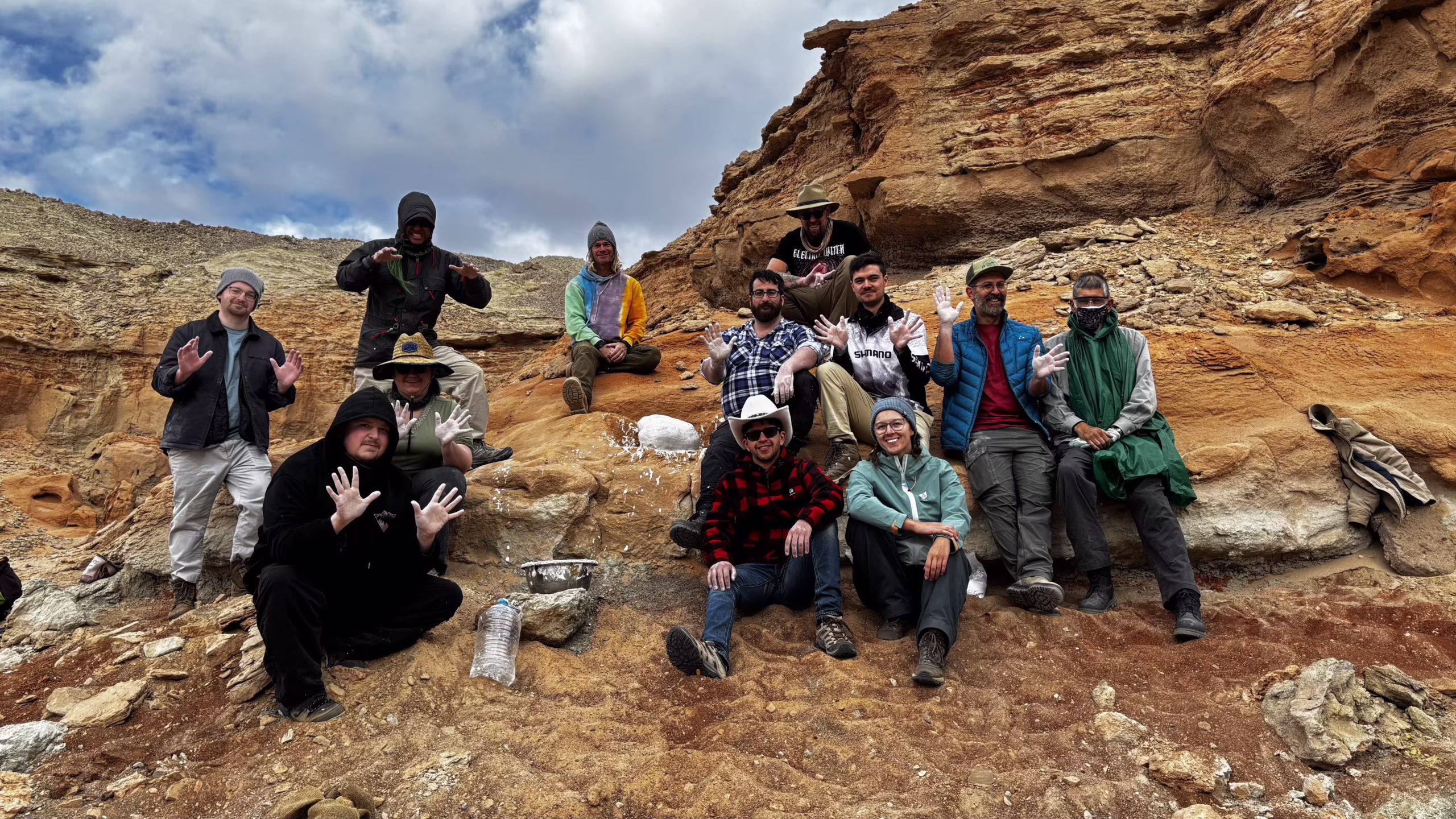 Group photo of the 2025 Lost Dinosaurs of the Gobi expedition participants sitting at a fossil excavation site after jacketing a fossil.